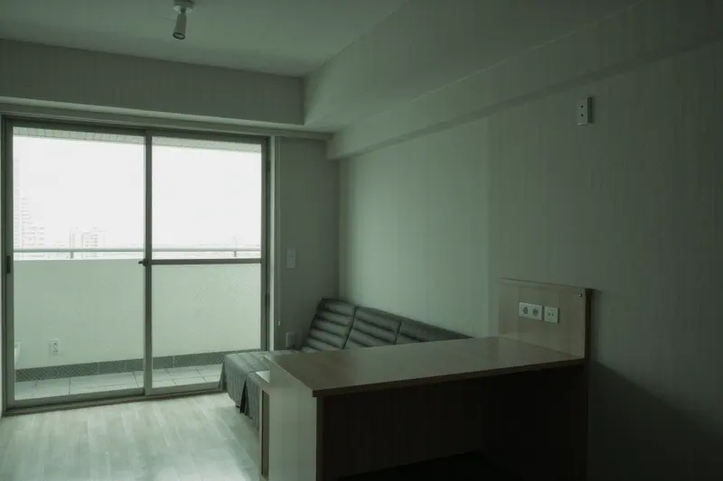 An empty flat with a bare desk, a folded sofa bed and a window onto a courtyard, floorboards swept and nothing on the walls.