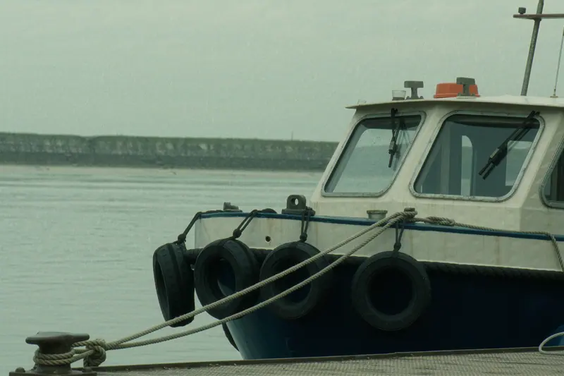A small passenger boat tied alongside a river pontoon with fenders out, flat grey water around it.